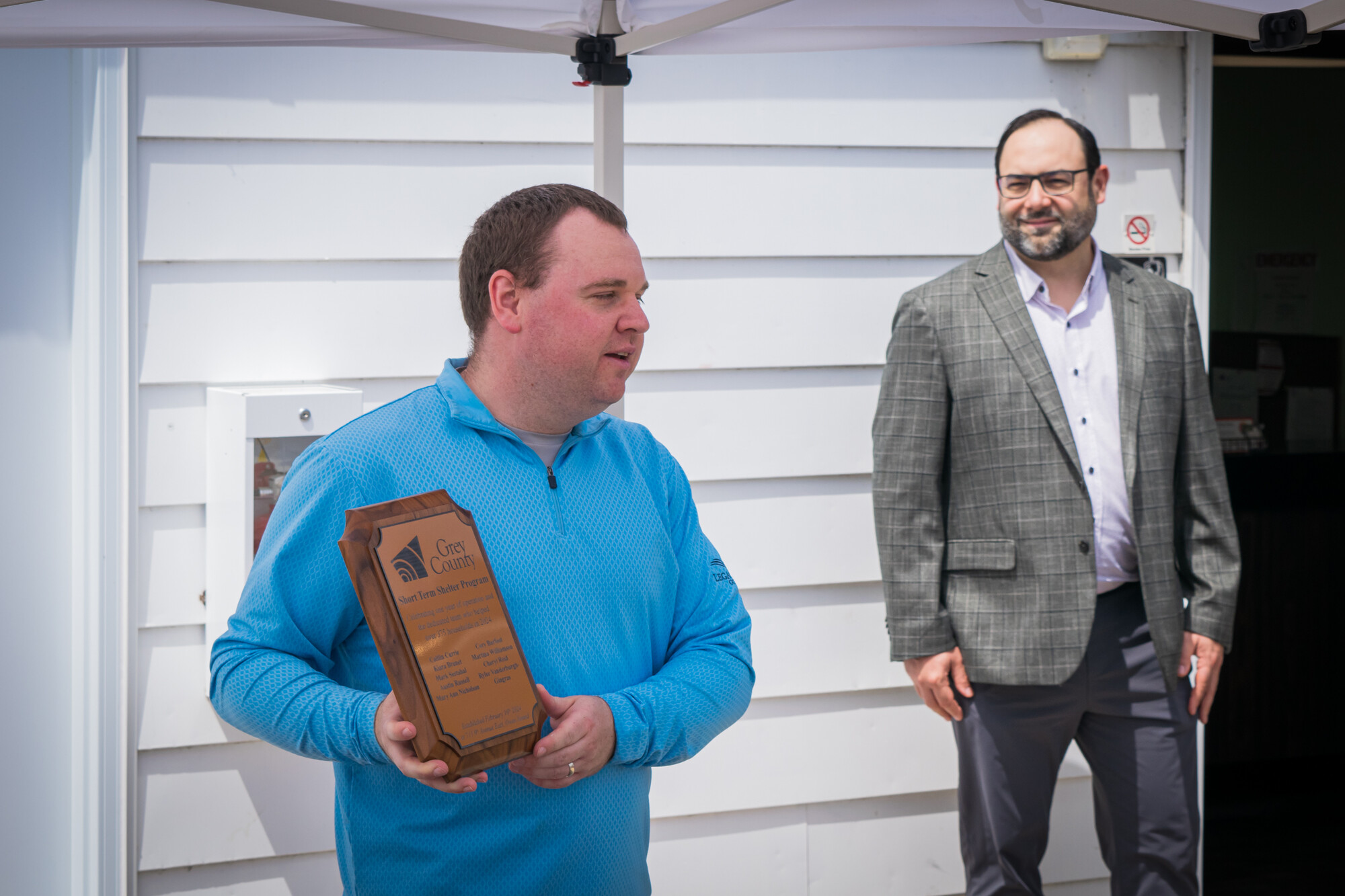 Josh Gibson, manager of housing programs, shares a commemorative plaque marking 1-year of operations of the motel-based emergency housing program. 