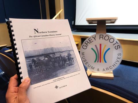 Volume 19 of the Northern Terminus Journal held in front of a podium in the Grey Roots Theatre.