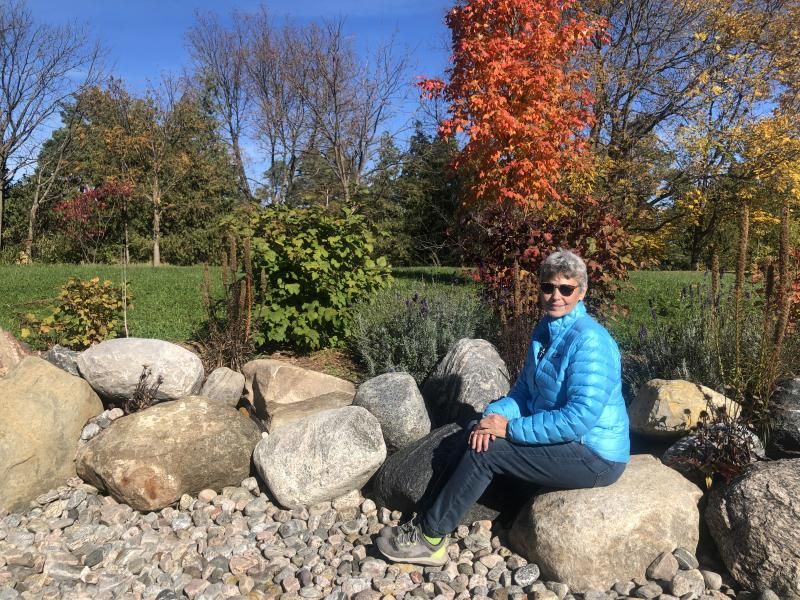 Alison sitting on a large boulder surrounded by native plants in her backyard