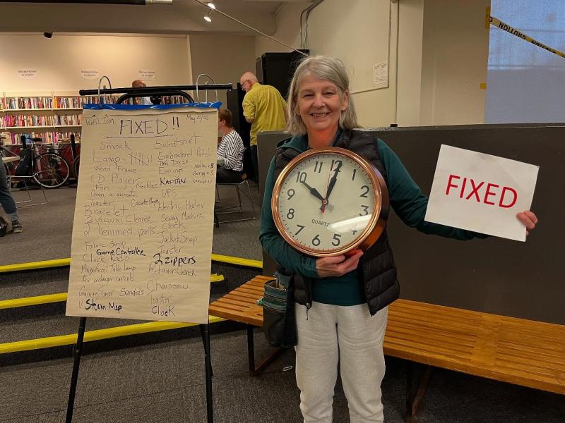 Older woman holding a clock and a "fixed" sign with a list of all the fixed items beside her