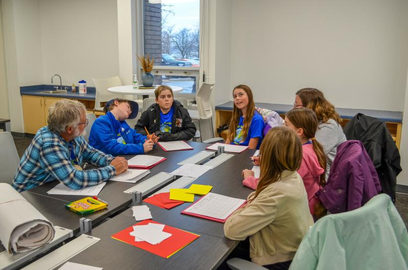 A group of students gathered around a table talking and writing
