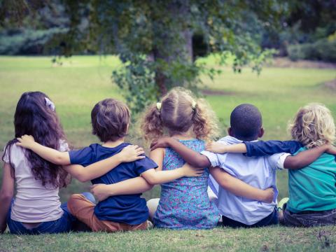 Five children locking arms in the park facing away from the camera