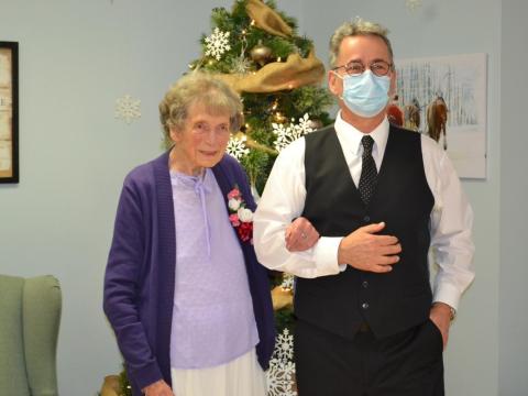 An elderly woman stands with her arm entwined with another gentleman in formal dance attire.