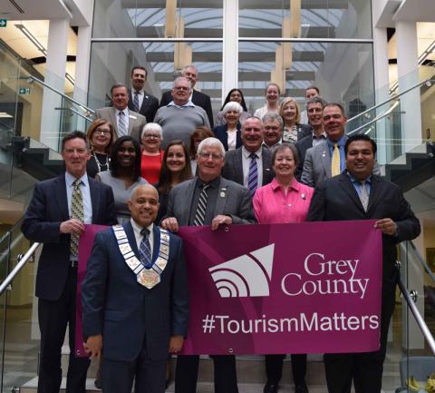 Members of council and Tourism staff hold the Tourism Week Banner on the steps in the Admin. Building