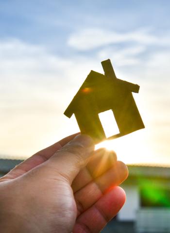 Image of a house cut out being held up to the sunset.