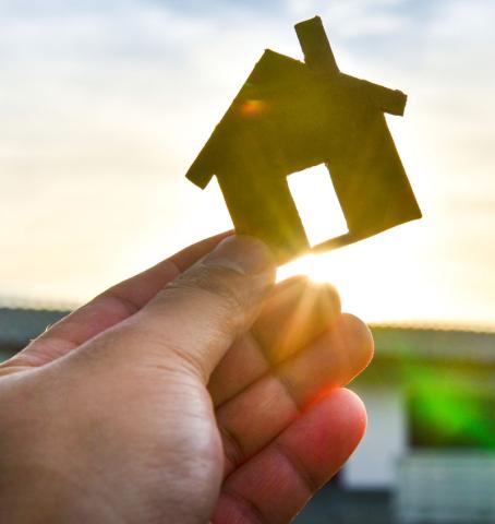 A cut out of a home is held up to the sun. 