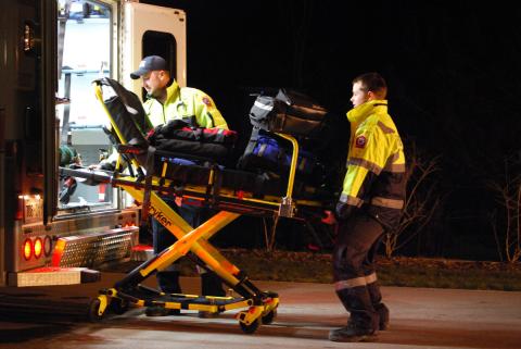 Two paramedics load a power lift stretcher into the back of an ambulance.