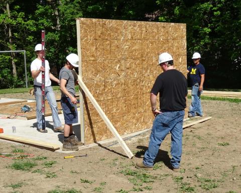 A group of volunteers work together to raise the first wall on pavilion.