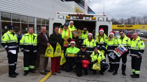 Paramedics, police officers and elected officials holding groceries in front of an ambulance.