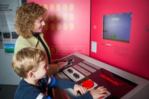 An adult and child play Super Mario Bros on a giant Nintendo controller.