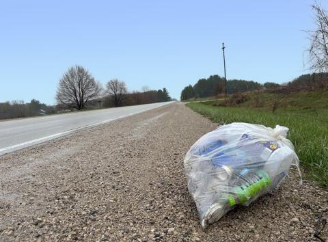 A clear bag of trash sitting on a roadside after being collected from the ditch.  