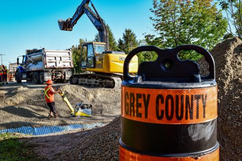 A Grey County pylon in front of an active construction zone with an excavator and dump truck