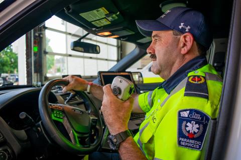 A uniformed Grey County paramedic holding the radio while sitting in the driver's seat of an ambulance.